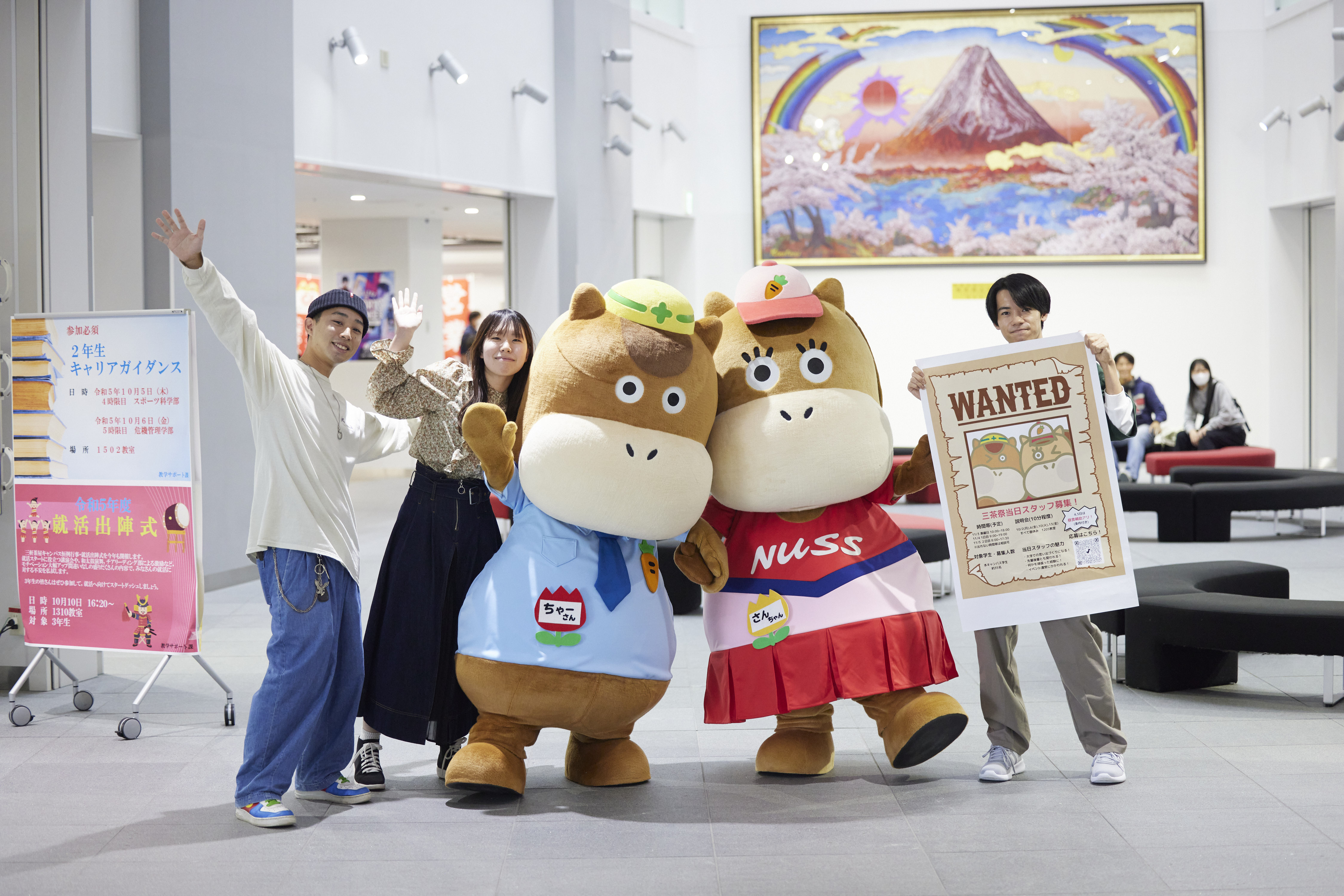 マスコットキャラクターと学生３名がポーズを取っている様子